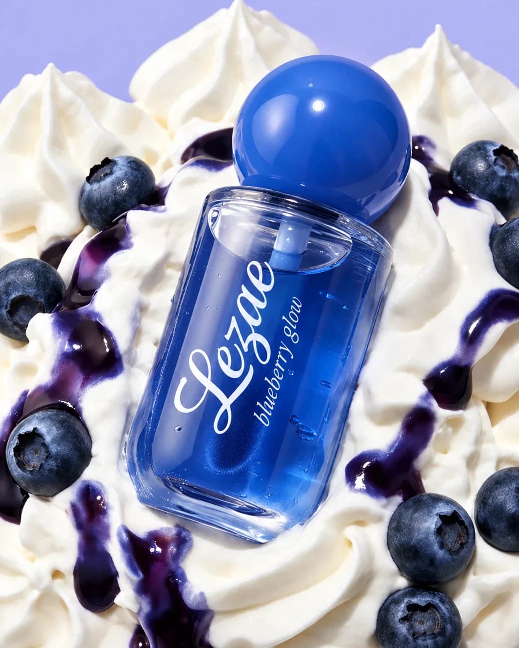 A product shot by EZZAR: a blue Lezae lip gloss bottle in whipped cream, among blueberries.
