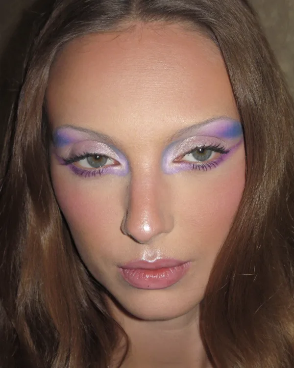 The shoot's model, a young woman in lilac make-up, photographed head on.